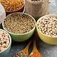 Various grains and seeds in colorful bowls with wooden spoons.