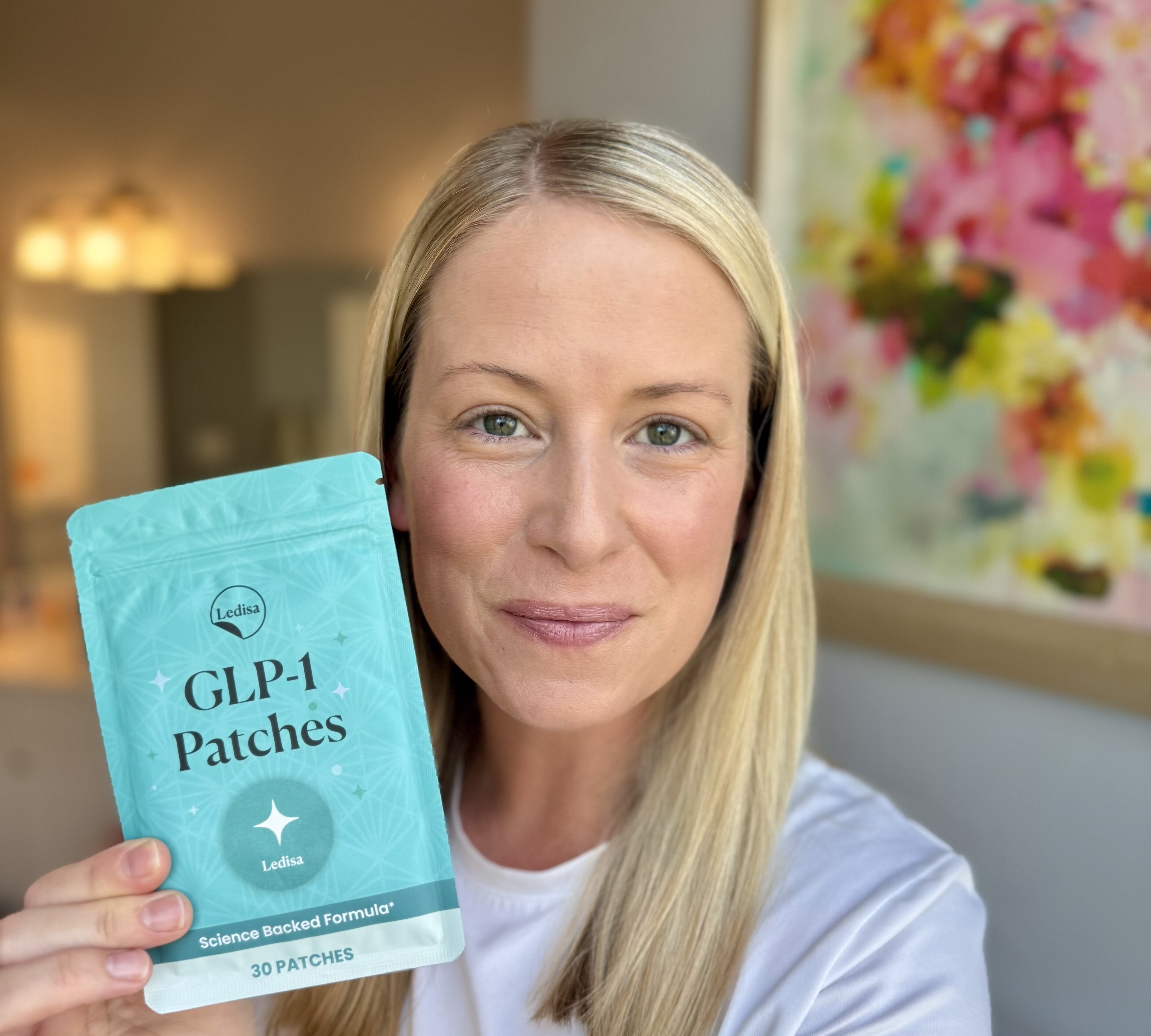Person holding a package of GLP-1 patches, smiling indoors.