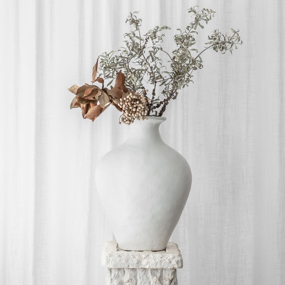 White vase with dried flowers on a textured pedestal.