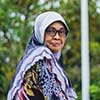 A woman wearing a patterned hijab and glasses looks toward the camera.