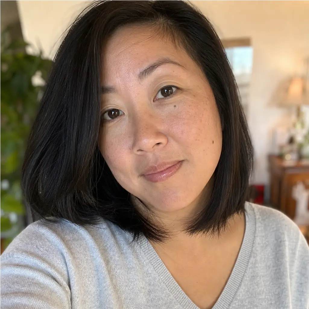 A woman with dark, shoulder-length hair and a grey sweater smiles slightly at the camera.
