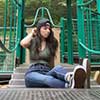 A woman with long dark hair wearing a backwards cap sits on a green playground structure.
