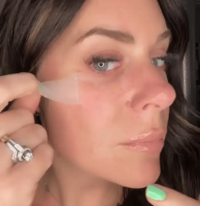 Person applying a transparent patch under their eye.