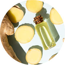 Slices of ginger and a small bottle of oil on a light background.