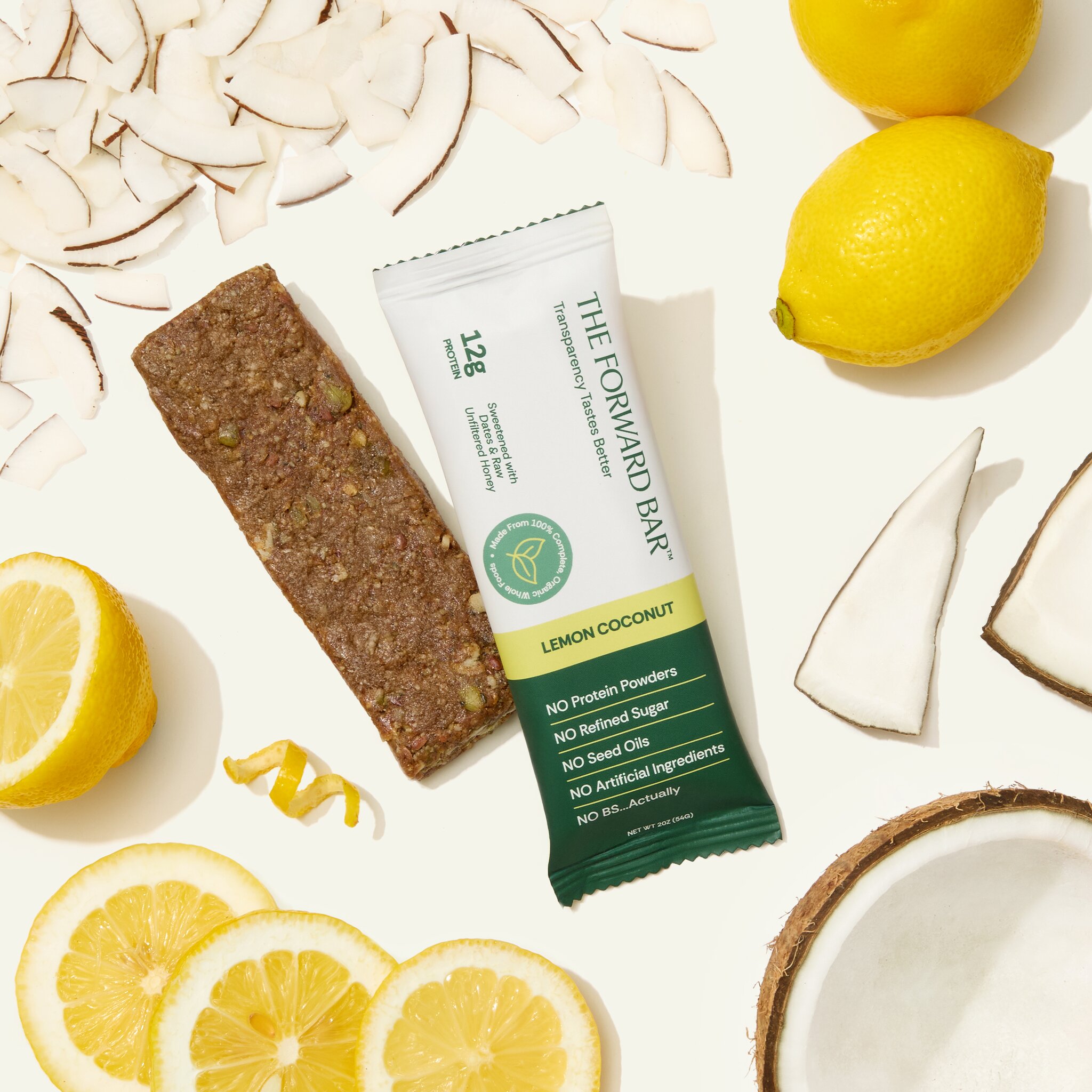 A Lemon Coconut Forward Bar protein bar is displayed with its ingredients, lemons and coconut, on a white background.
