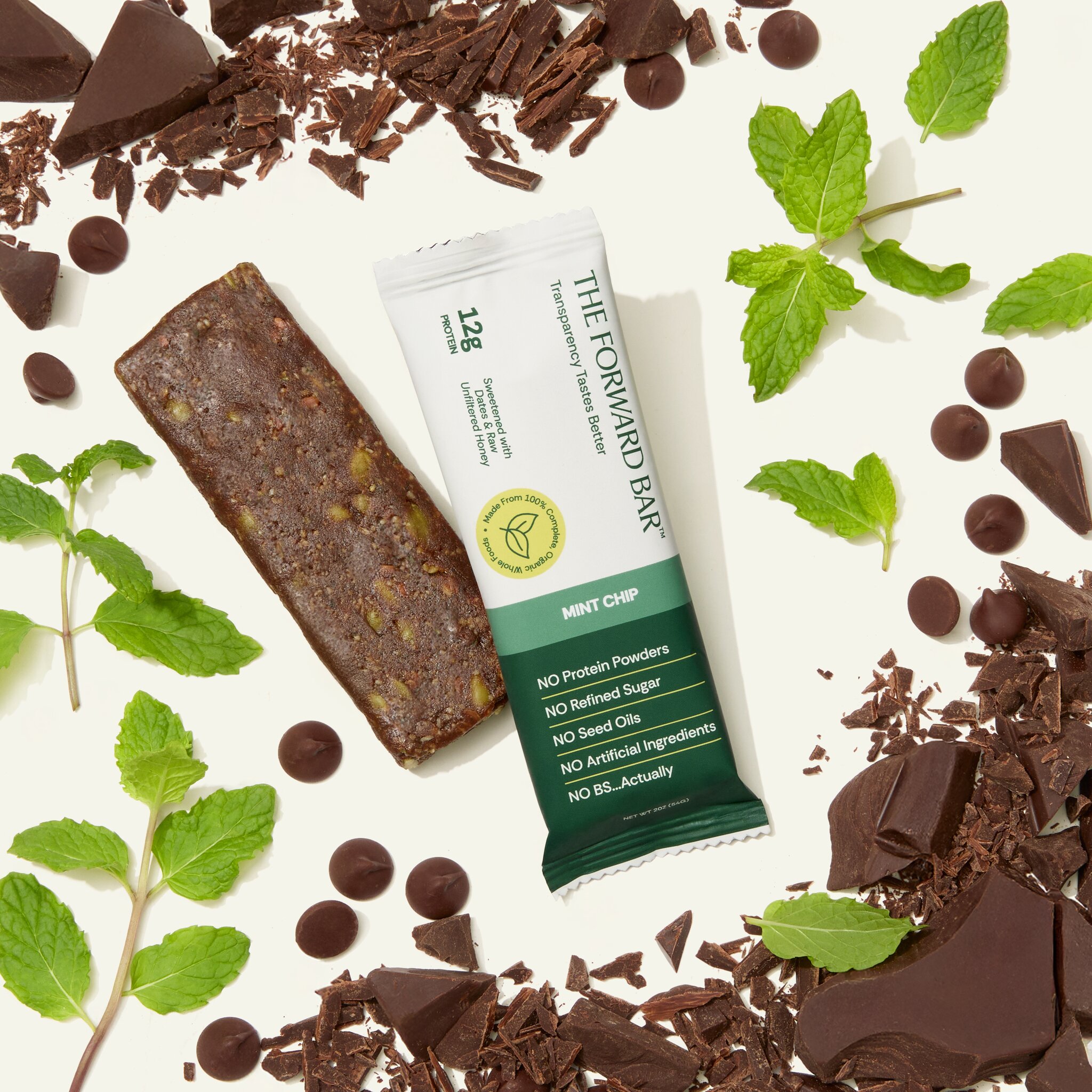 A Forward Bar Mint Chip protein bar surrounded by fresh mint leaves and pieces of dark chocolate.