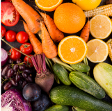 Assorted fruits and vegetables, including oranges, tomatoes, carrots, grapes, and cucumbers on a dark surface.