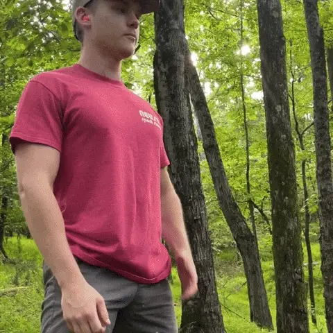 Person in a red shirt standing in a forested area.