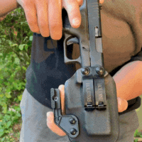 Person holding a handgun in a holster outdoors.