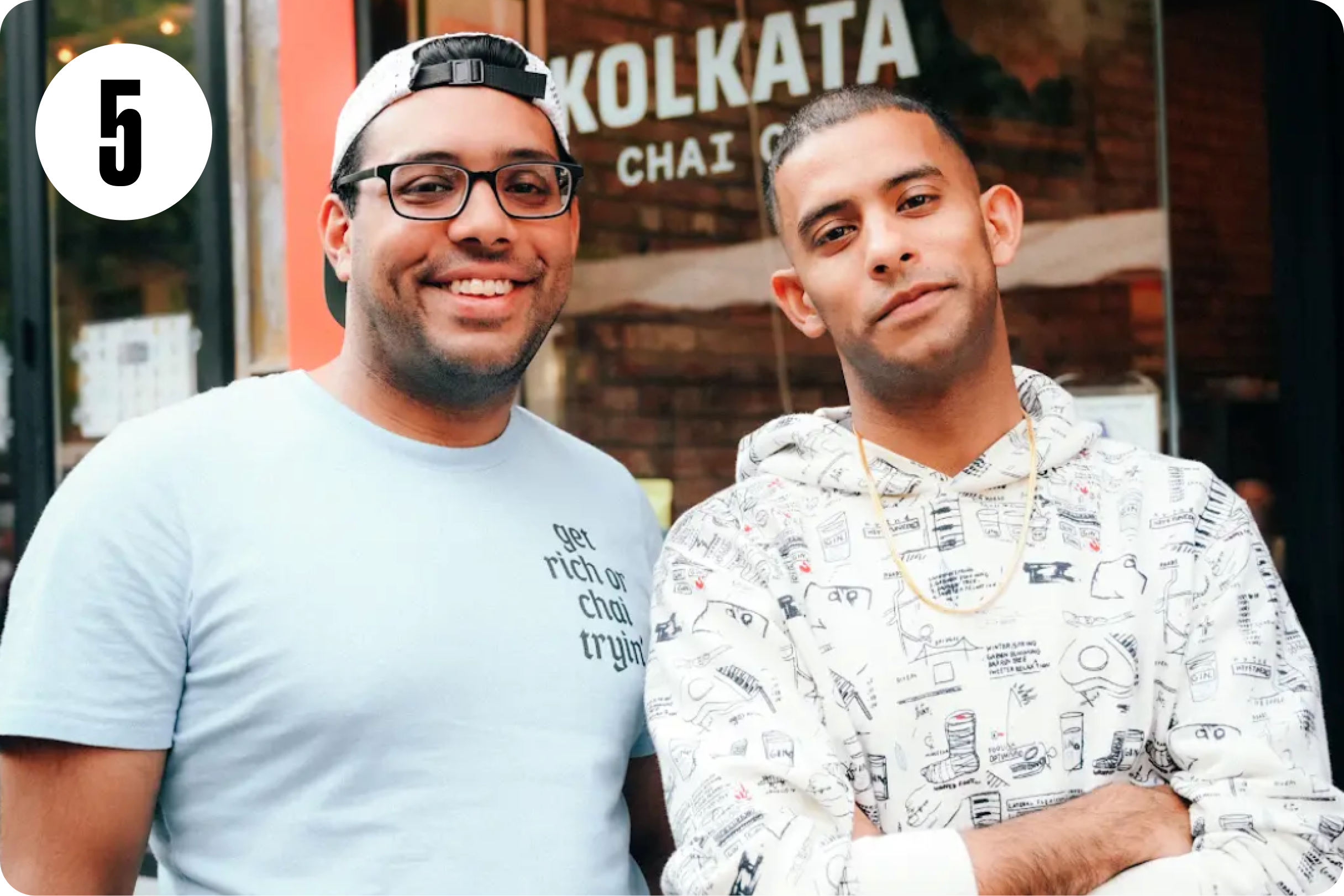Two men smiling in front of a Kolkata Chai Cafe sign.