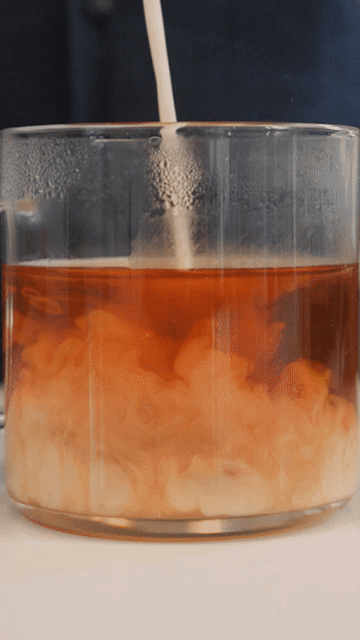 Milk swirling into a glass of tea.