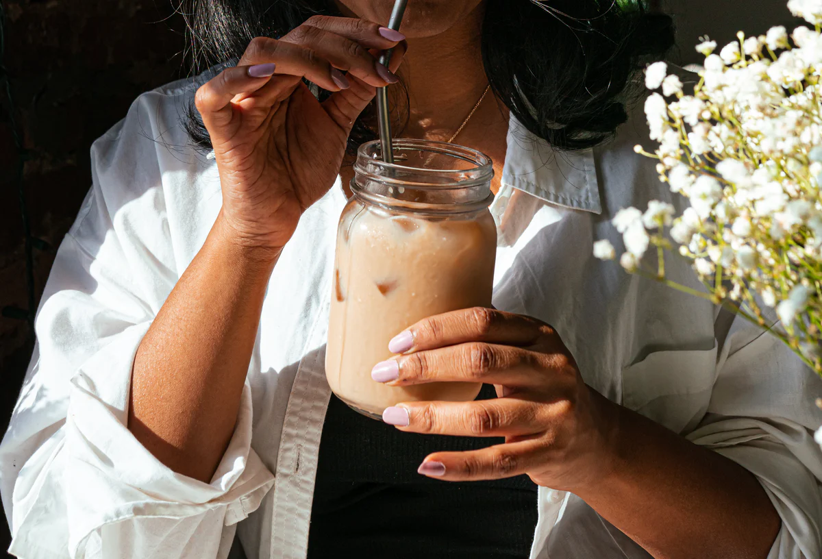 A person in a white shirt sips an iced drink from a mason jar through a metal straw.