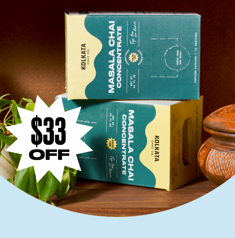 Masala chai concentrate boxes with $33 off sticker, wooden texture, and plant nearby.