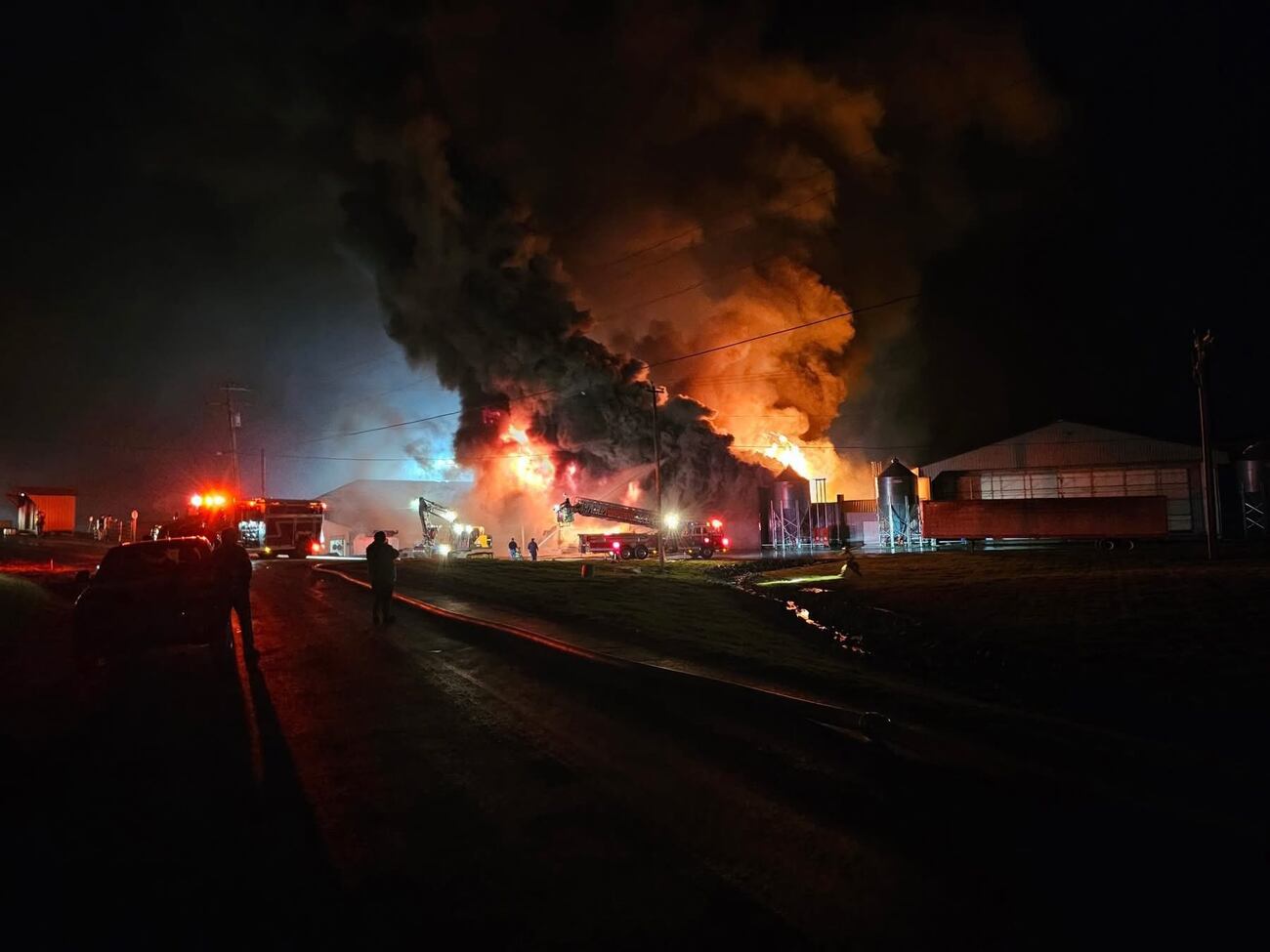 At night, a large building is engulfed in flames and smoke as firefighters respond.