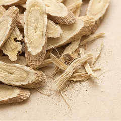 A close-up of sliced dried woody roots, some fibrous, on a light brown textured surface.