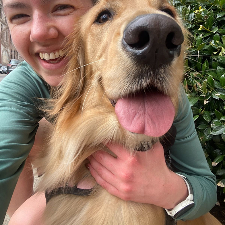 A close-up selfie of a smiling woman hugging a happy-looking golden retriever.