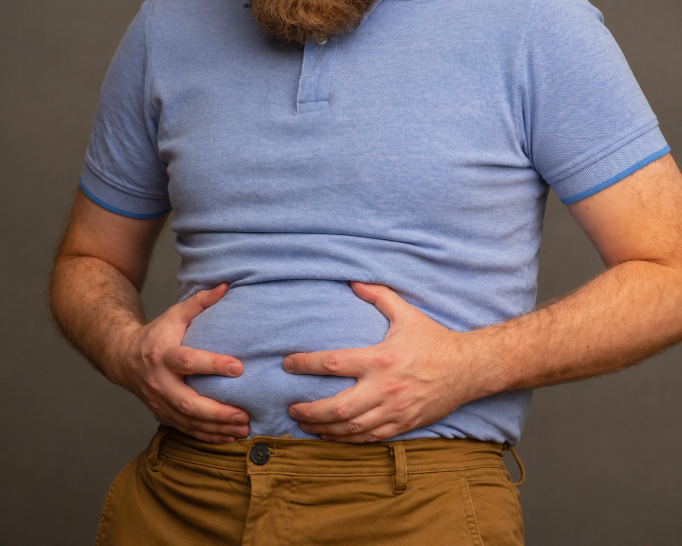 A man in a blue polo shirt and brown pants holds his belly with both hands.