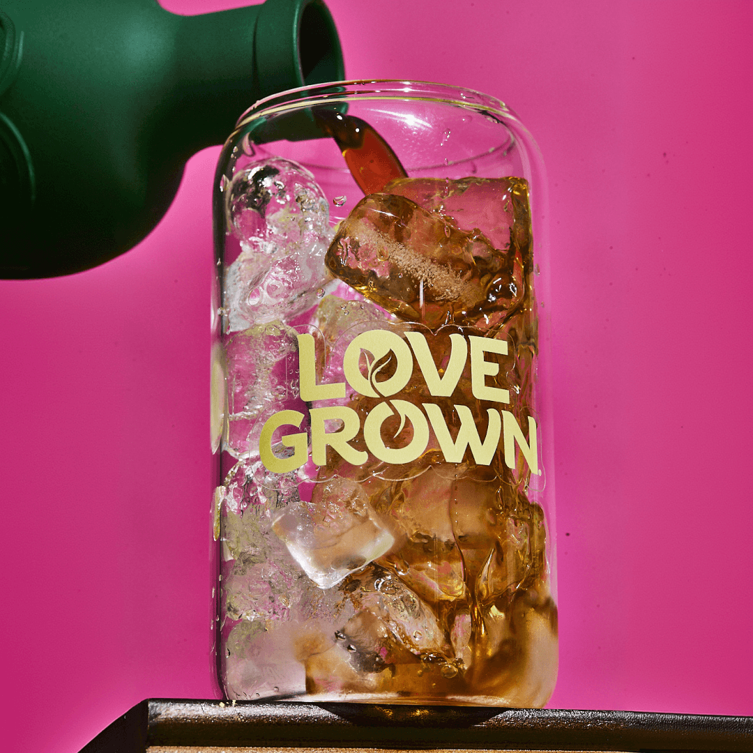 A dark liquid is poured from a green bottle into a glass with ice and 'LOVE GROWN' text.
