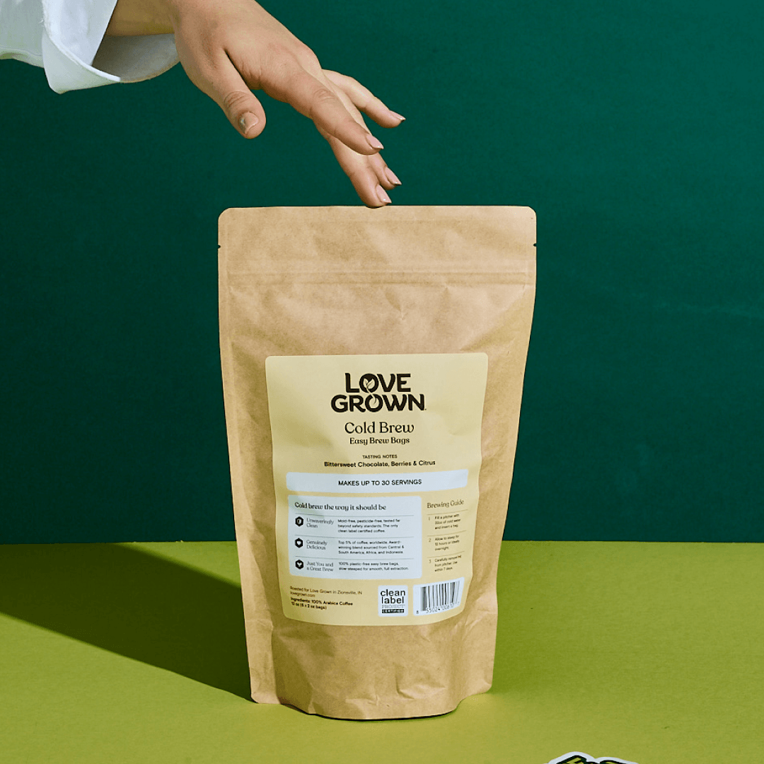 A hand reaches for a bag of Love Grown Cold Brew coffee against a green background.