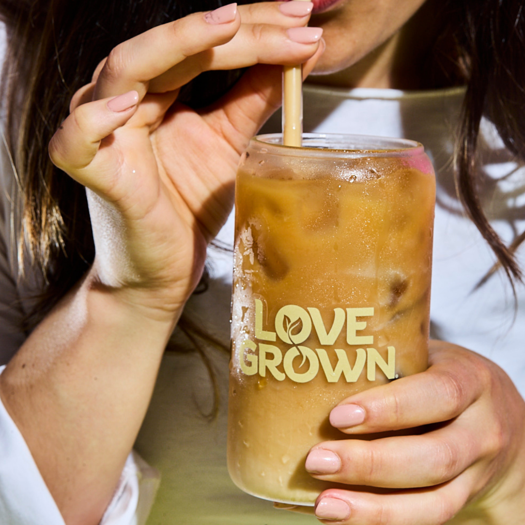A person drinks an iced coffee from a glass with a “LOVE GROWN” logo on it.