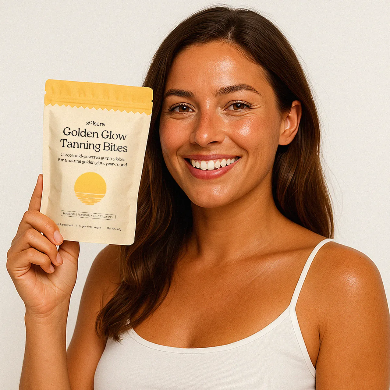 Smiling woman holding a package of Golden Glow Tanning Bites.