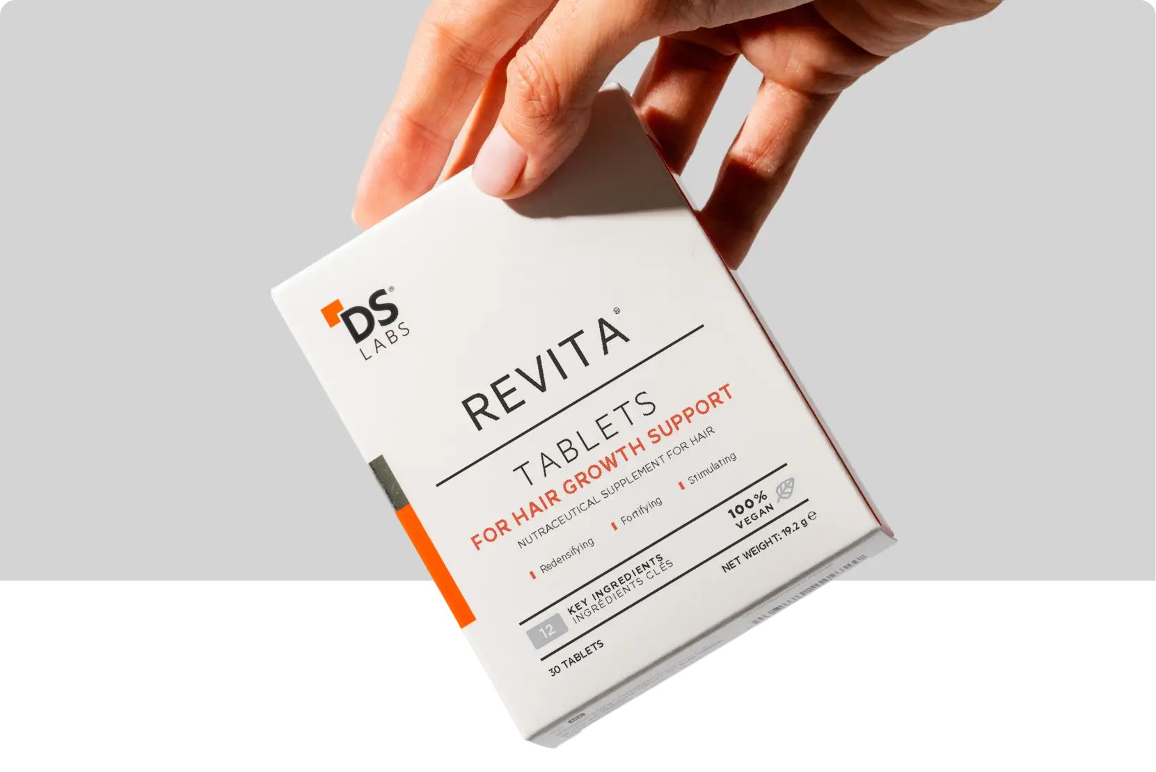 Hand holding a box of Revita hair growth support tablets.