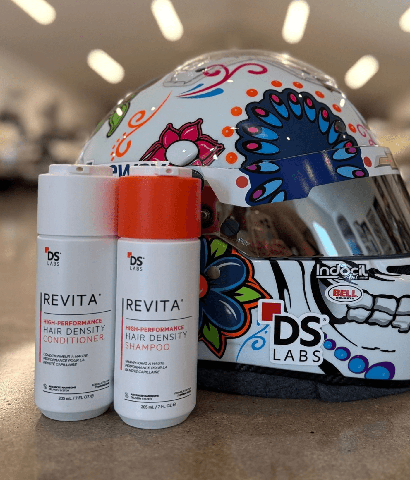 DS Labs Revita shampoo and conditioner bottles sit in front of a colorfully decorated racing helmet.