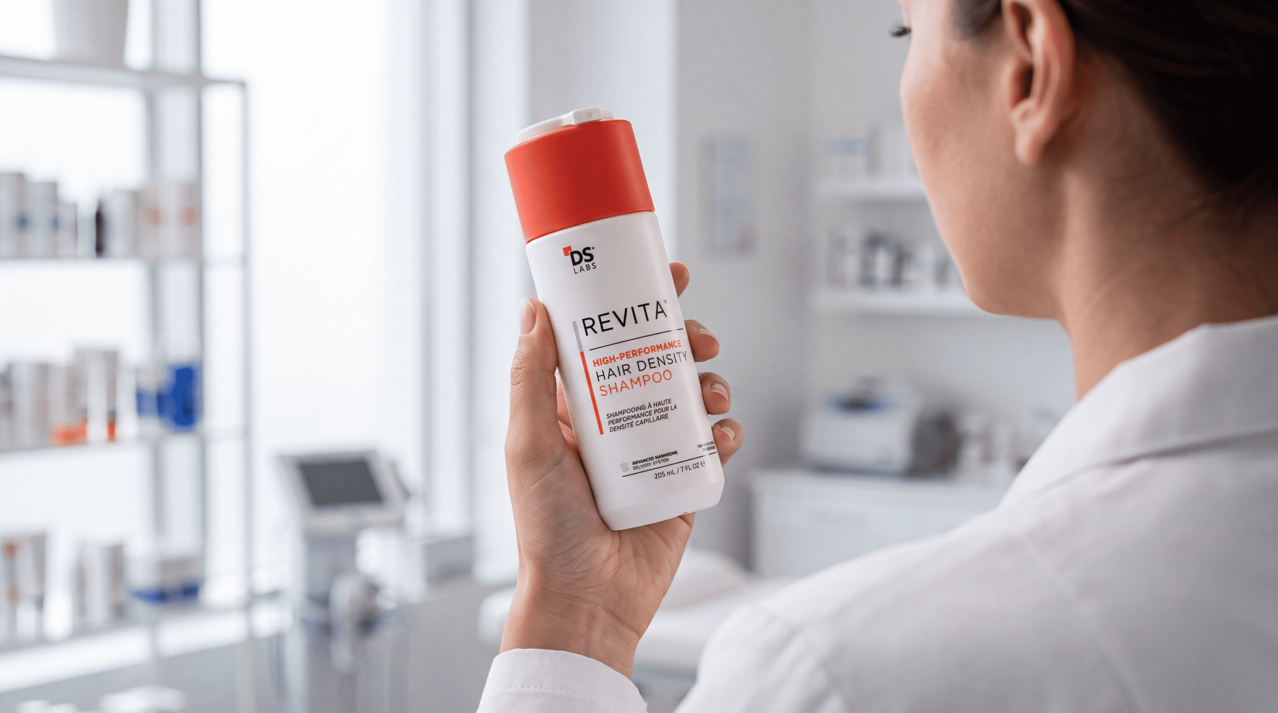 A person in a white coat holds a bottle of Revita High-Performance Hair Density Shampoo.