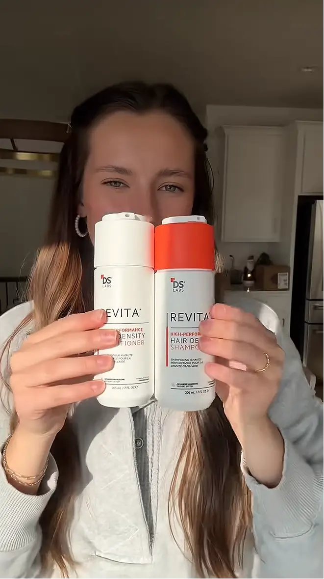 A woman holds up two bottles of Revita hair care products, a shampoo and a conditioner.