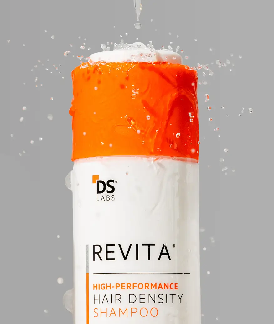 Revita shampoo bottle with orange cap and water droplets on gray background.