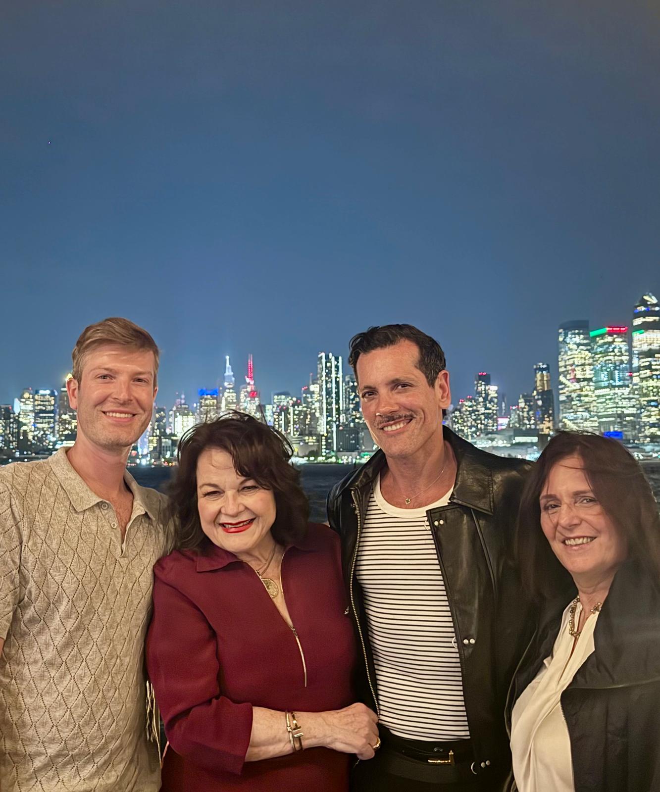 Four people smiling for a photo in front of a brightly lit city skyline at night.