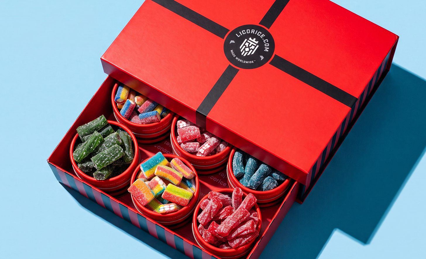 An open red gift box from Licorice.com filled with several small bowls of assorted colorful, sugar-coated candies.