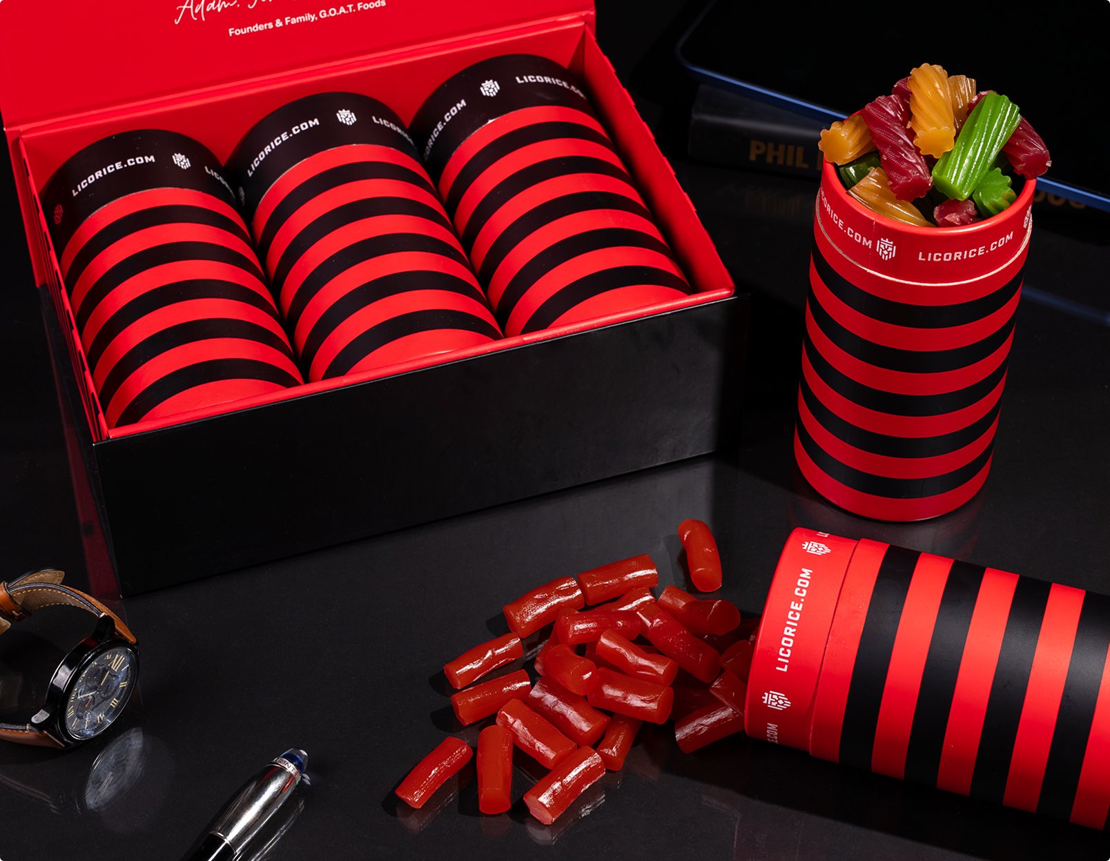 A gift box of licorice.com candy with red and black striped containers on a black tabletop.