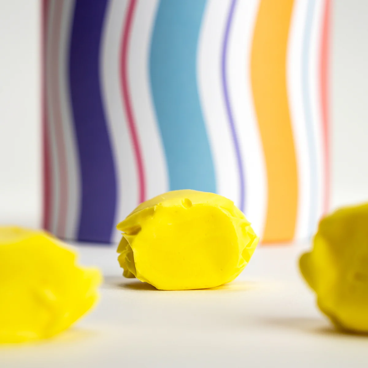 Yellow candies on a white surface with a colorful striped background.