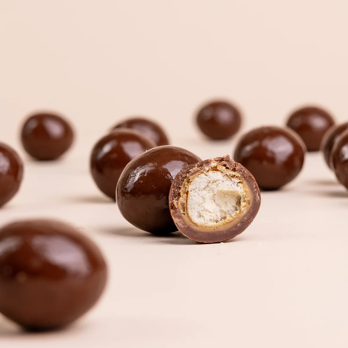 Chocolate-coated snacks on a beige surface, one with a bite showing the interior.
