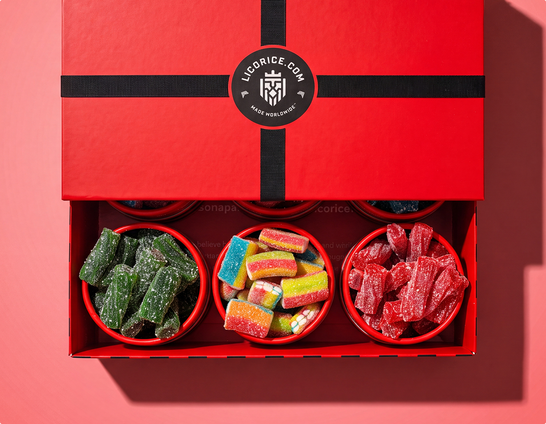 An open red gift box from Licorice.com revealing three bowls of colorful, sugar-coated licorice candies.
