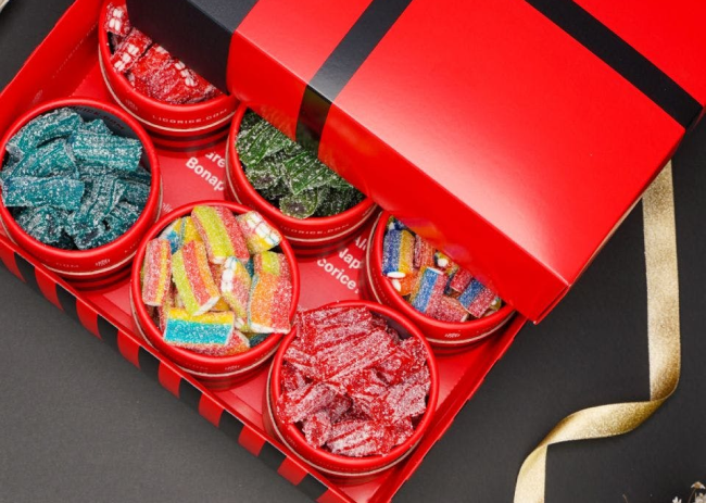 Box of colorful assorted candies in red containers.