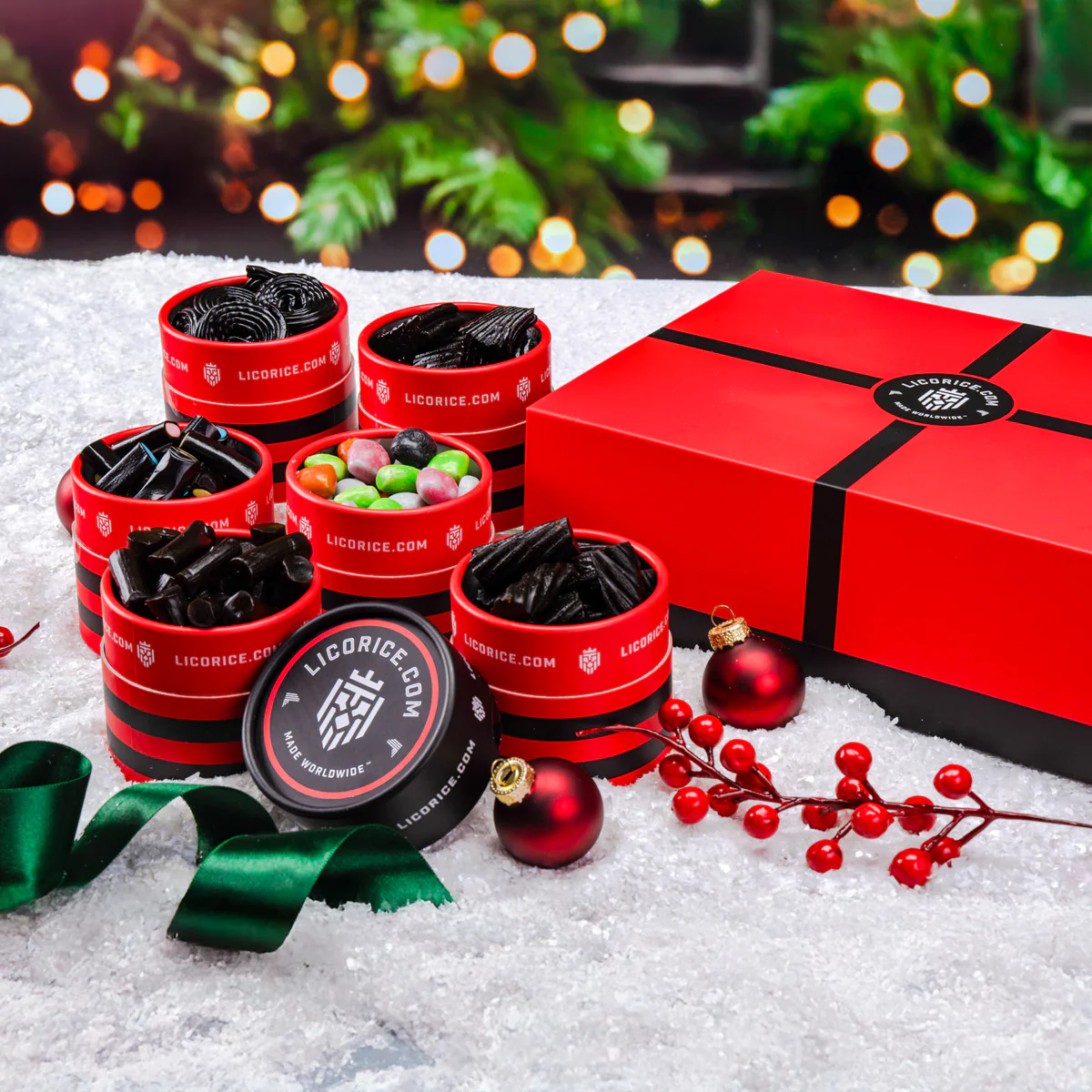 Red licorice containers with holiday ornaments on snow.