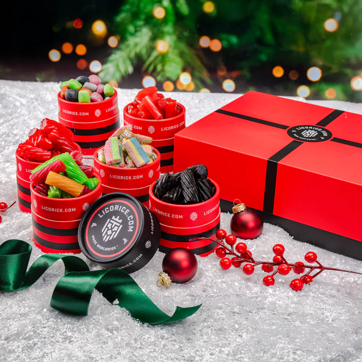 Red containers of licorice and candies on snowy surface with a gift box and ornaments.