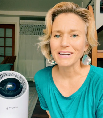 A person in a teal shirt sits near a white Sterra device indoors.