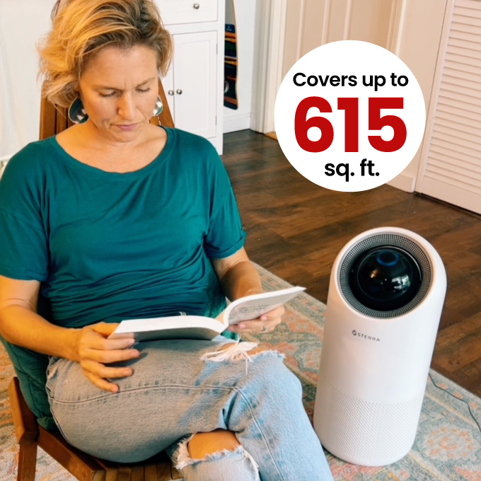 Person reading near an air purifier with text 'Covers up to 615 sq. ft.'