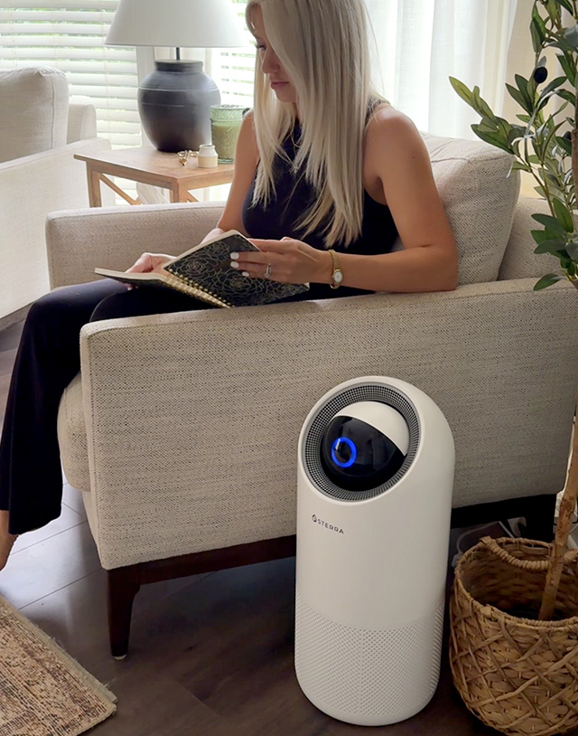 Woman reading on a couch beside a white air purifier.