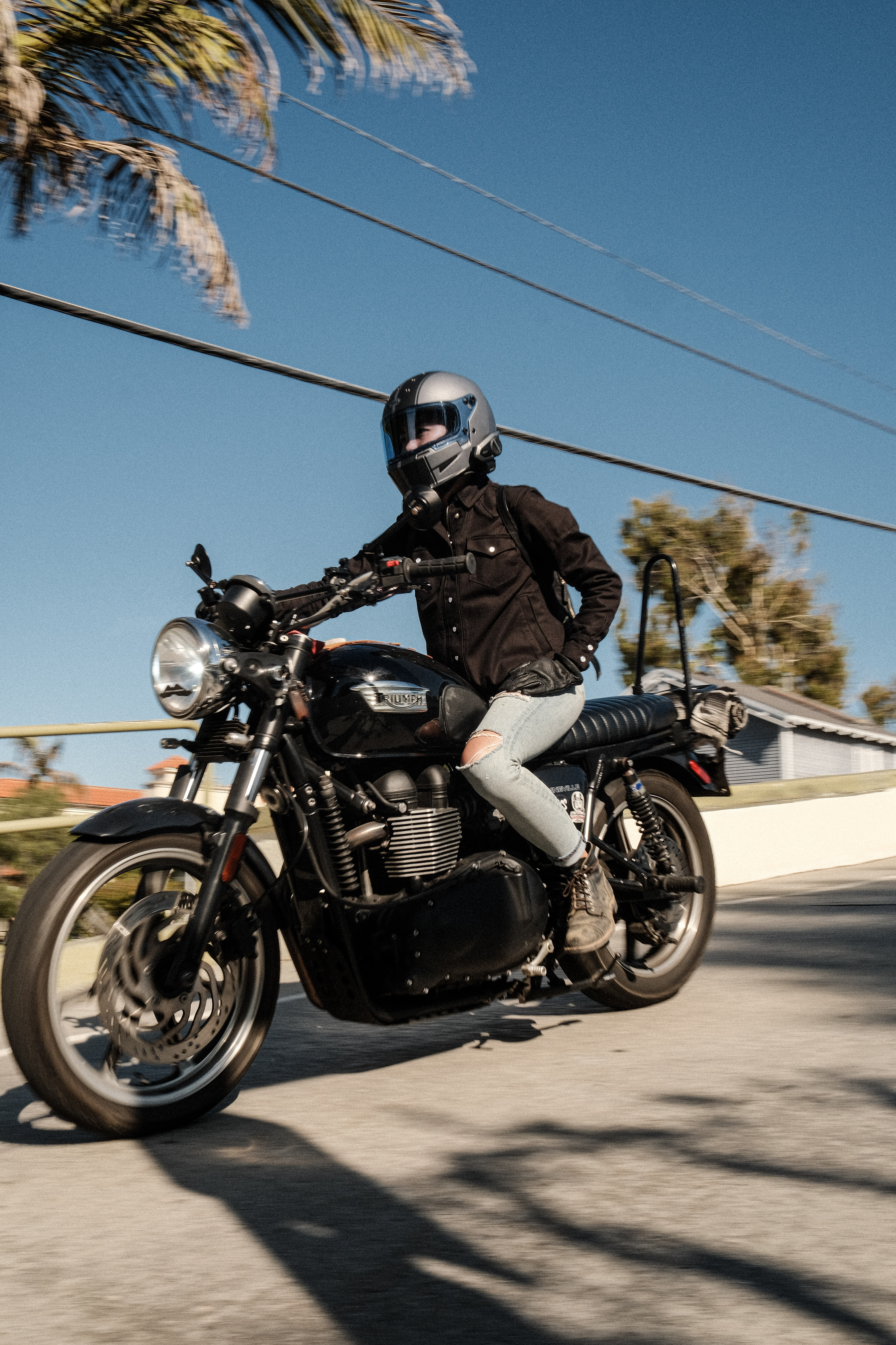 Person riding a motorcycle on a sunny day with palm trees in the background.