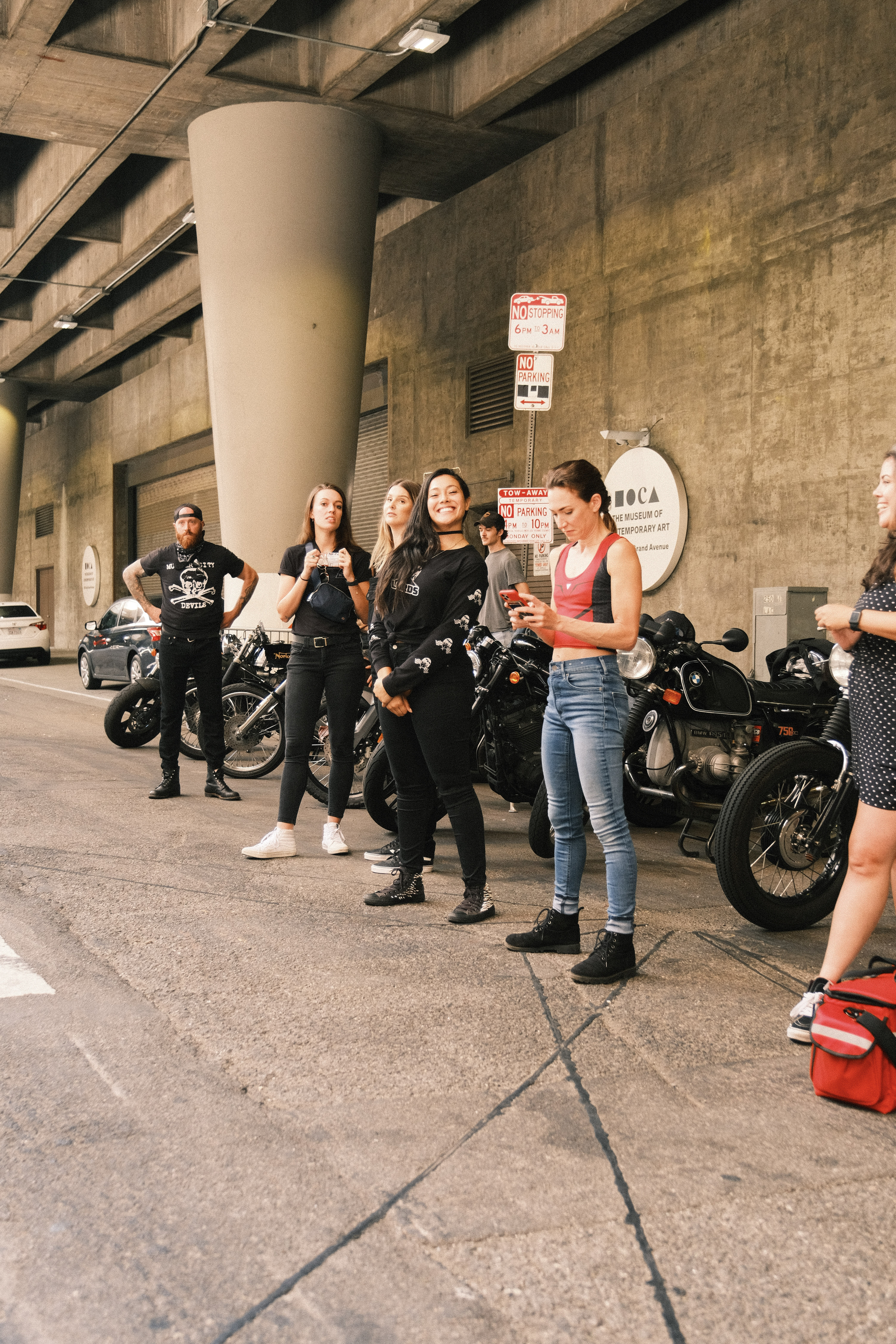 Group of people standing near motorcycles under a concrete structure.