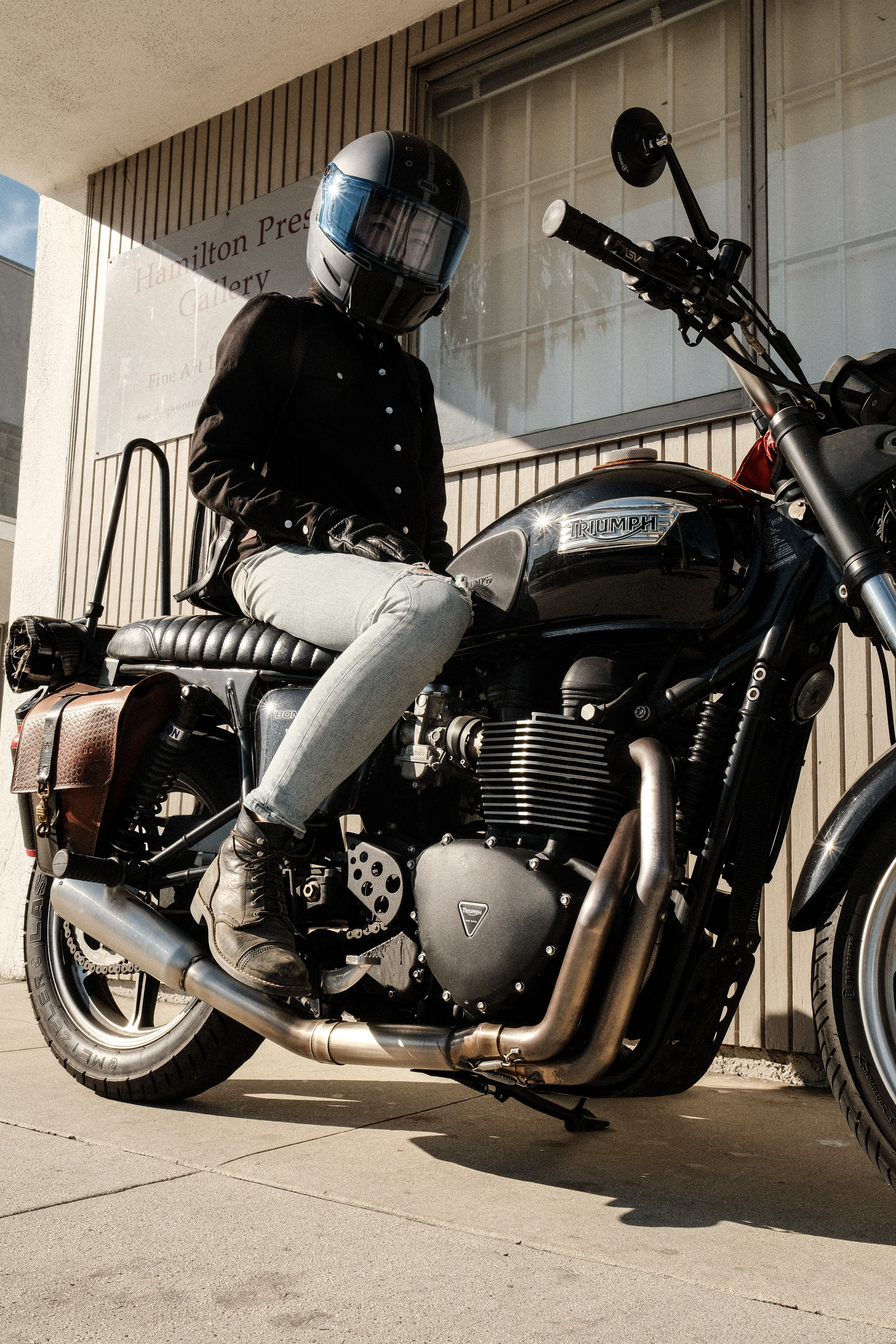 Person in helmet sitting on a Triumph motorcycle outside a building.