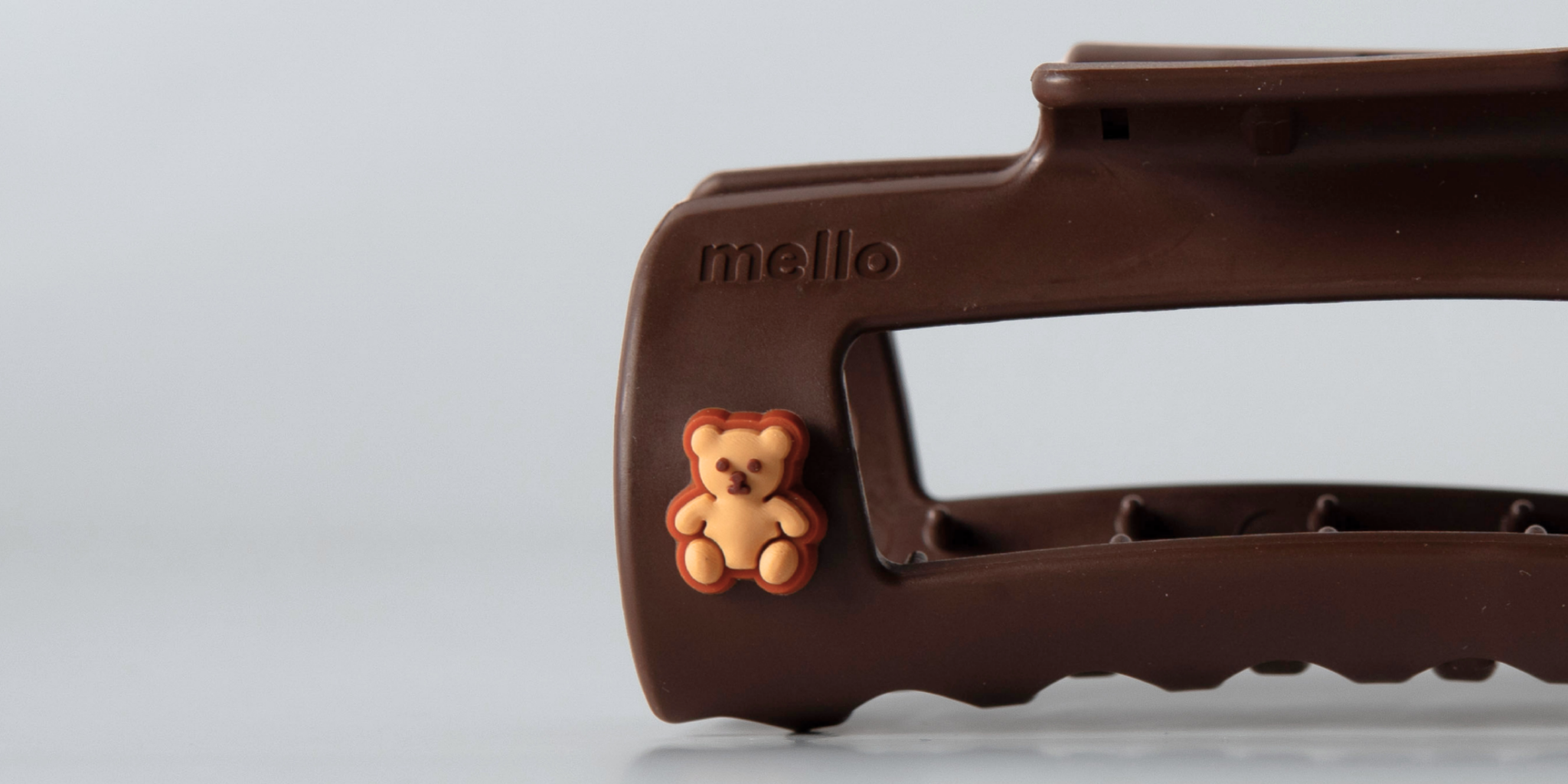 A close-up of a brown hair clip with a small teddy bear decoration and the word 'mello'.