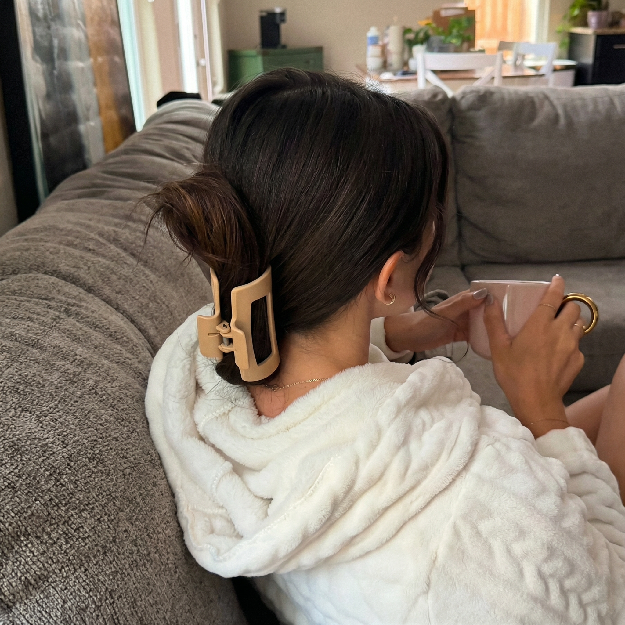 Person with hair clip drinking from a mug on a couch.