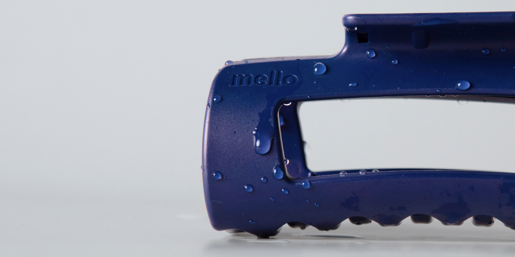 A close-up of a blue Mello hair clip covered in water droplets against a plain, light-colored background.