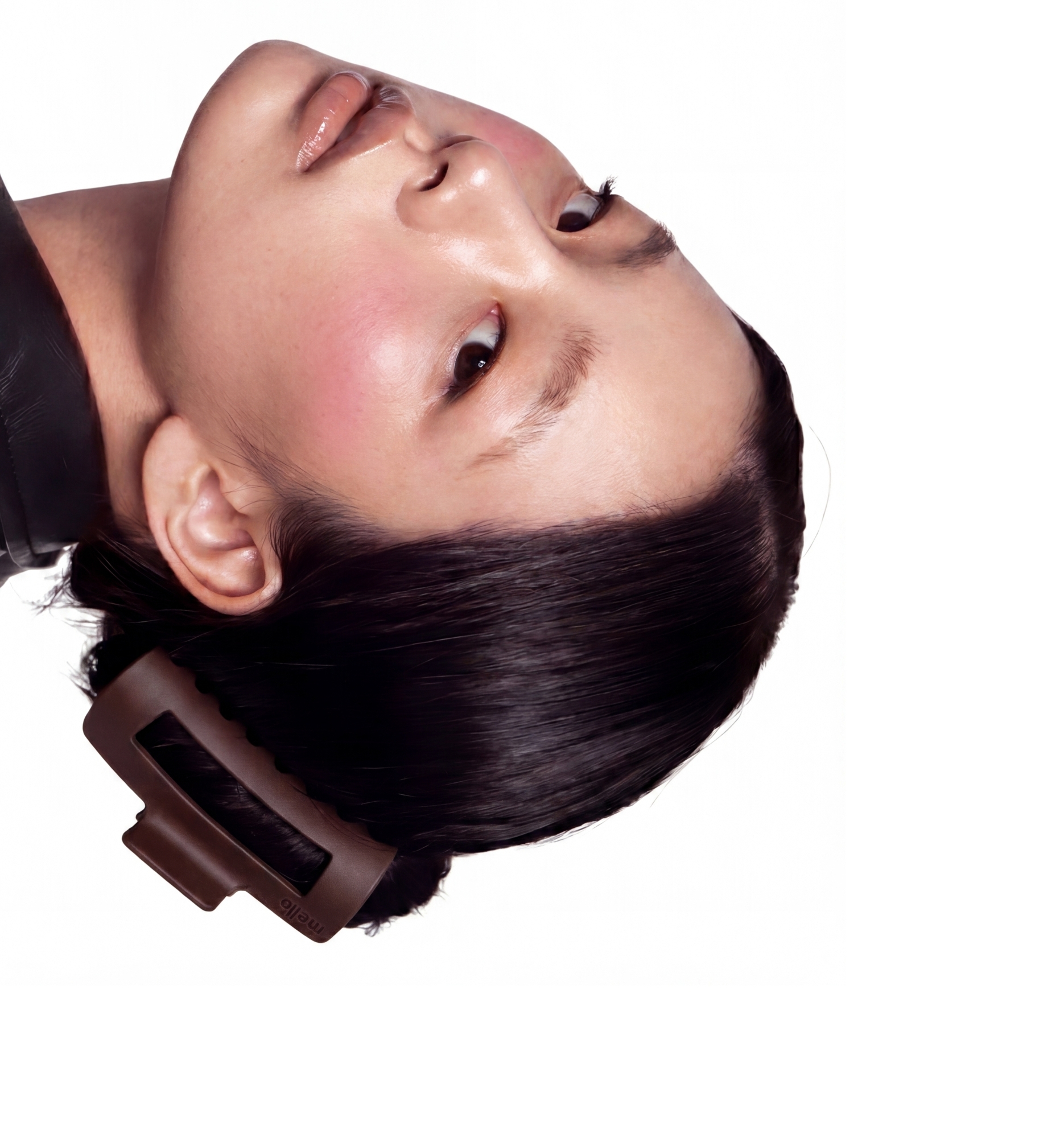 A close-up of a person's face tilted sideways, with dark hair held by a brown clip.