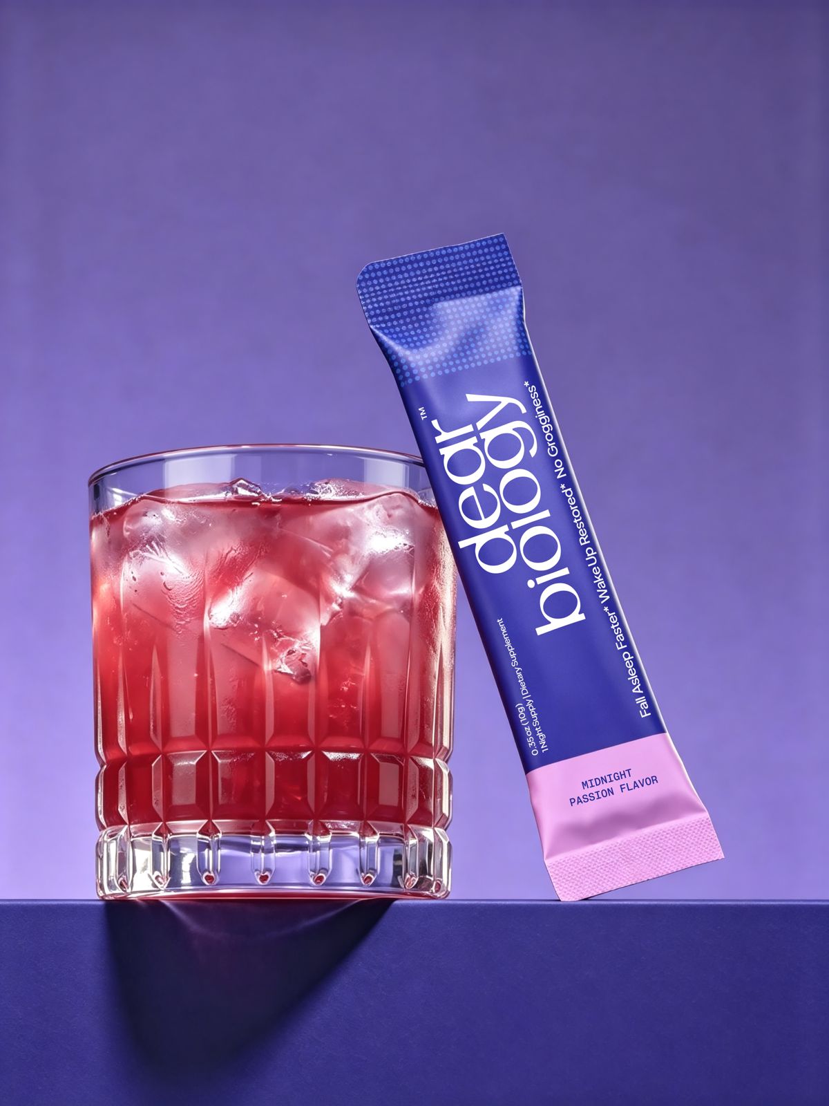 A glass of red iced drink next to a 'dear biology' Midnight Passion Flavor supplement packet.